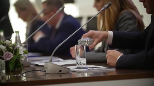 Primo piano colpo di mani di persone durante la discussione alla riunione della conferenza. Bottiglie d'acqua e bicchieri sui tavoli. versare acqua nel bicchiere — Video Stock