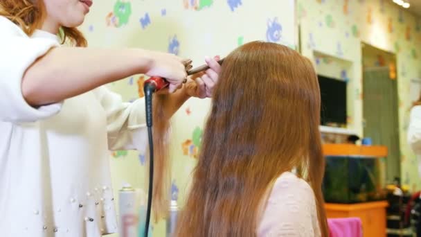 Stylist is curling lange haren voor kind meisje, met behulp van elektrische krultang — Stockvideo
