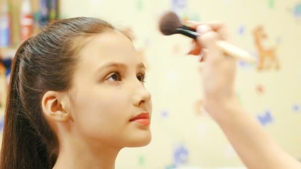 Maquiagem artista faz com que o pó no rosto de uma jovem. Fechar — Vídeo de Stock