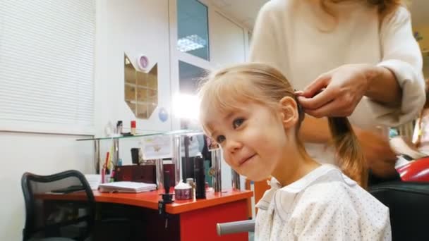 Kinderfriseursalon. Friseur mit kleinem blonden Mädchen. Lustiges Kind im Friseursalon. Pferdeschwanz reparieren. — Stockvideo
