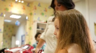 Elektrik kıvırmak demir kullanarak küçük sevimli kız için kıvırma ve cumbing uzun saç stilist olduğunu.