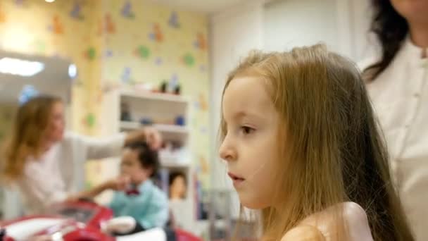 Stilist elektrik kıvırmak demir kullanarak küçük sevimli kız için uzun saç kıvırma. Arka plan üzerinde küçük çocuk — Stok video