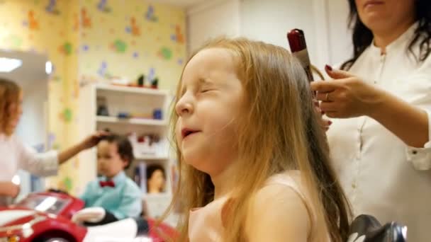 Estilista es rizado pelo largo para niña linda, utilizando rizador eléctrico. Niño en el fondo. Slider tiro — Vídeo de stock