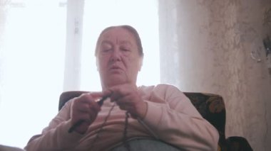 Yaşlı bir kadın bir sandalyede oturuyor ve pencerenin arka plan üzerinde örgü