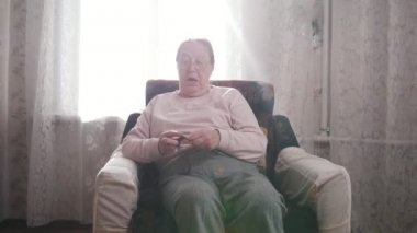 Yaşlı bir kadın bir sandalyede oturuyor ve parlayan pencere arka plan üzerinde örgü sahiptir. Portre