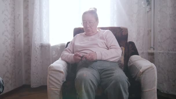 年配の女性が椅子に座っていると、ウィンドウの背景に編み物趣味を楽しんでいます. — ストック動画
