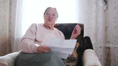 Yaşlı bir kadın bir sandalyede oturuyor ve pencerenin arka plan üzerinde yüksek sesle okuyarak.