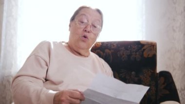 Yüksek sesle okuyarak pencerenin arka plan üzerinde bir sandalyede otururken yaşlı bir kadın.