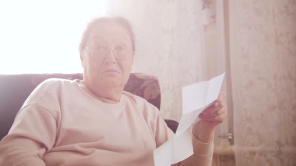 Una donna anziana leggere lettera mentre seduto su una sedia sullo sfondo della finestra . — Video Stock