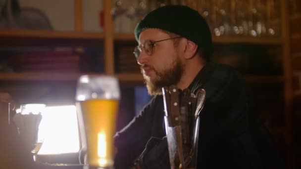 Homem barbudo de óculos a beber cerveja no bar — Vídeo de Stock