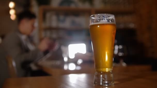 Bärtiger Mann mit Brille im Gespräch mit seinem Freund in der Bar. Restaurant. Fokus auf Glas Bier — Stockvideo