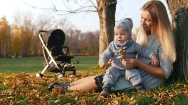 Genç çimde oturma ve onun küçük bebek tutan anne. Park. Güneş ışığı.