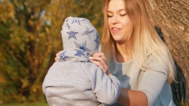 Junge Mutter, die mit ihrem kleinen Baby auf dem Gras sitzt und ihn hält. Reparatur seiner Kleidung — Stockvideo