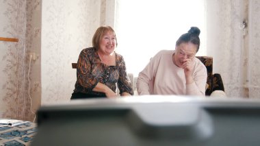 İki yaşlı kadın TV izlerken, birbirlerine bakıyor ve gülüyor. Portre