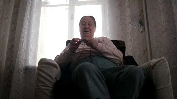 Пожилая женщина сидит в кресле и вяжет на заднем плане окна, улыбаясь — стоковое фото