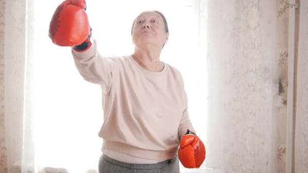 Une vieille femme âgée boxe avec des gants rouges, souriant — Photo