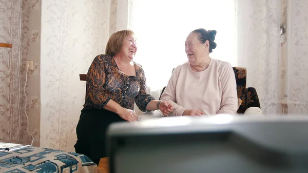 Две пожилые женщины смотрят телевизор, смотрят друг на друга и смеются. — стоковое фото