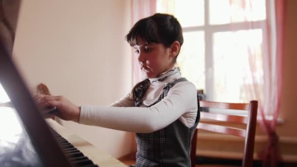 Una niña sentada junto a un piano y la cierra — Vídeo de stock
