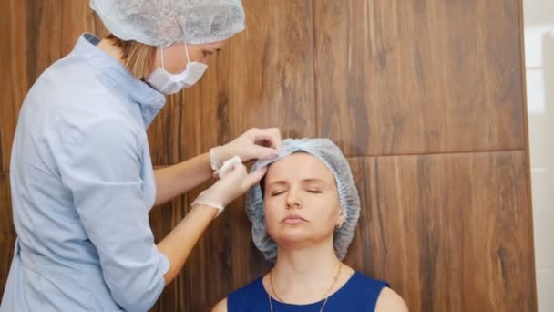 Vrouw in een kliniek cosmetologie. Specialist veegt client gezicht — Stockvideo