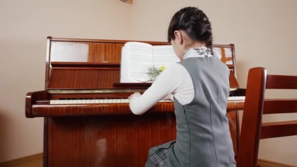 Музичний урок. Дівчина грає на піаніно. Вид повзунка, що грає ззаду дівчини — стокове відео
