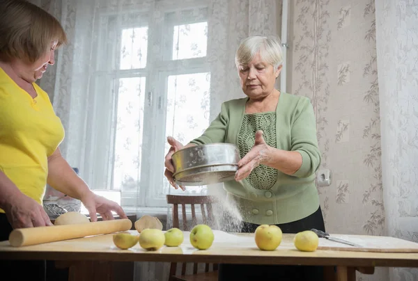 Две пожилые женщины делают маленькие пирожки. Просеивание муки — стоковое фото