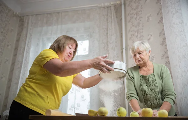 Dos ancianas haciendo tartas de manzana en casa. Tamizar la harina — Foto de Stock