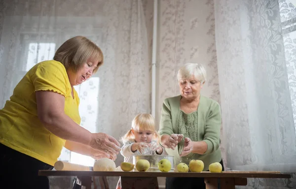 Две пожилые женщины делают яблочные пирожки дома. Просеивание муки с маленькой блондинкой — стоковое фото