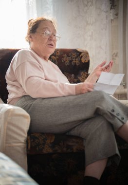 Meşgaleleri. Gözlüklü yaşlı bir kadın onun hobi bir koltukta oturan ve pencerenin arka plan üzerinde harfleri okuma sahiptir.