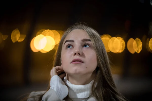 Portrait of young woman in the subway waiting for the train. Looking up, hand on the neck. Back lights.