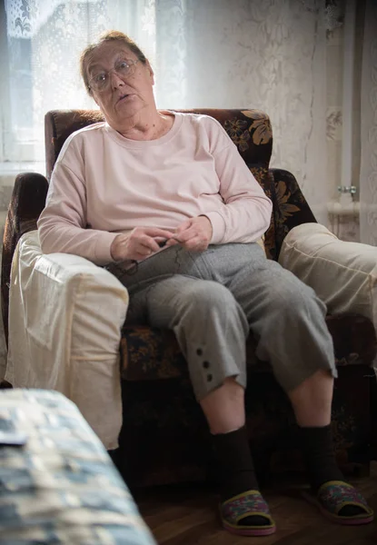 Passatempos. Uma mulher caucasiana idosa desfruta de seu hobby sentado em uma poltrona e tricô no fundo da janela . — Fotografia de Stock