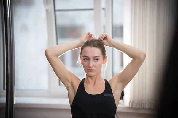 Joven mujer atractiva en sujetador deportivo en estudio de entrenamiento pone su cabello en cola de caballo —  Fotos de Stock