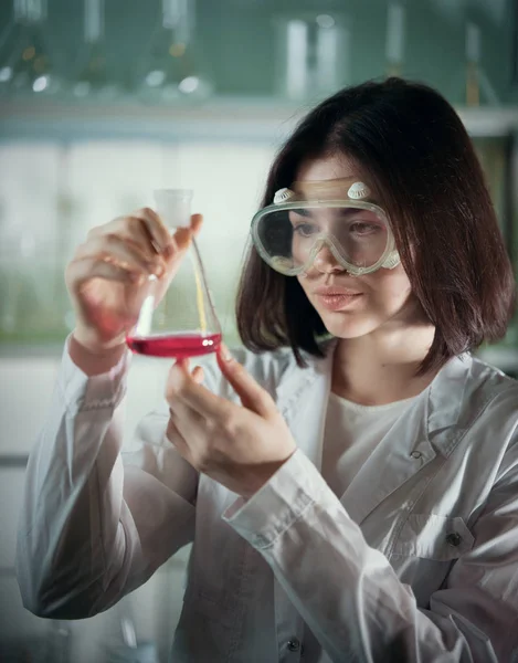 Laboratorio químico. Mujer joven en gafas de trabajo mirando el frasco —  Fotos de Stock
