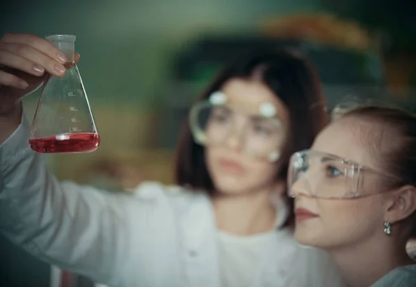 Laboratorio químico. Dos mujeres jóvenes sosteniendo un frasco con líquido rojo en él —  Fotos de Stock