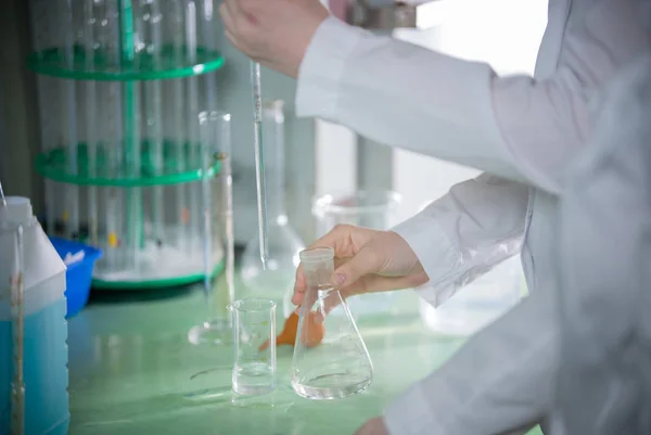 Laboratorio químico. Mujer joven sosteniendo un frasco, transfundir algo usando pipeta — Foto de Stock