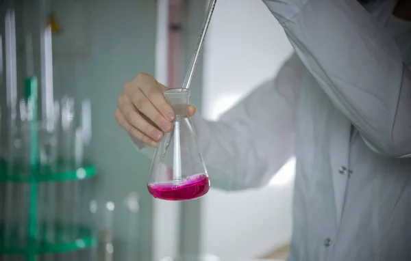 Химическая лаборатория. Молодая женщина держит фляжку, капает что-то с помощью пипетки. Жидкость стала розовой — стоковое фото