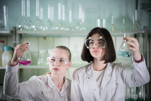 Chemielabor. zwei junge Frauen, die verschiedene Fläschchen mit Flüssigkeiten in sich tragen. Blick auf den Kolben — Stockfoto