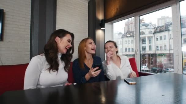 Трое молодых женщин в кальяне сидят у телефона и смеются — стоковое видео
