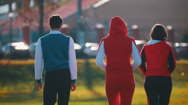 Mensen in kostuums van de sport wandelen in het park. Terug hoek — Stockvideo
