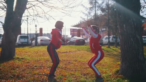 Duas jovens em trajes esportivos fazendo agachamentos e pulando no parque — Vídeo de Stock