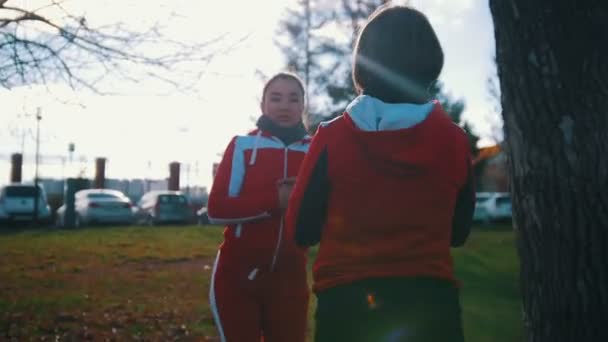 Dvě mladé ženy v kostýmech sport dělat dřepy v parku před sebe — Stock video