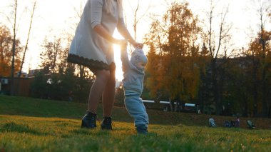 Genç Anne ve küçük bebeği sonbahar parkta yürümeyi öğretim.