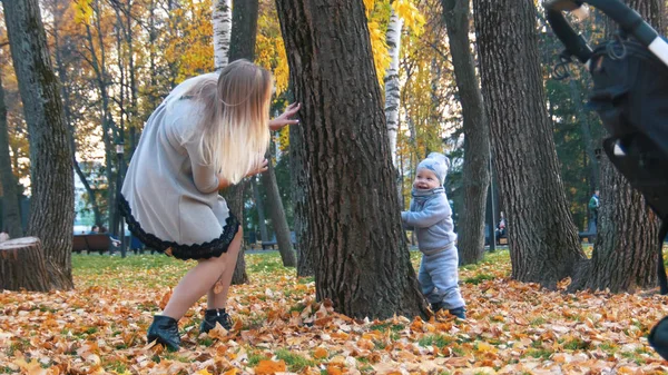 Ung mamma och hennes lilla bebis i parken. Spela Dölj och söka nära trädet — Stockfoto