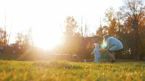 Ung mamma och hennes lilla bebis som spelar i höstens park på sunset — Stockfoto