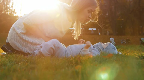 Молодая мать и ее маленький ребенок играют в парке. Ребенок лежит на траве — стоковое фото
