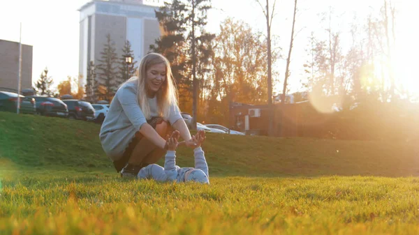 Ung mamma och hennes lilla bebis som spelar i parken. Det barnet som ligger på gräset. Mor röra babys händer — Stockfoto