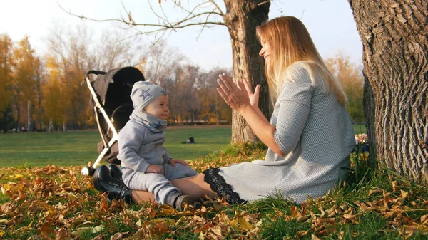 Joven madre jugando con su pequeño bebé riendo en el parque de otoño — Foto de Stock