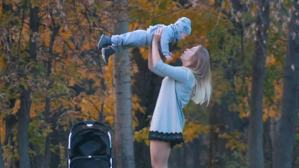 Glad ung mor med blont hår som håller upp hennes baby — Stockfoto