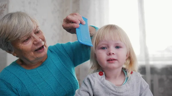 Nagymama élvezi a fésülködés a haj, a gyermek napsütéses reggel. Jó idő otthon. — Stock Fotó