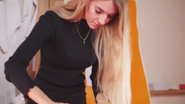 Junge Frau mit Armprothese in der Näherei, die Skizzen auf dem Tuch anfertigt. Nähgarn im Fokus. — Stockvideo