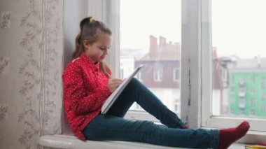 Pencere kenarında oturan ve çizim bir kız